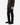 A person is shown from the waist down, standing against a plain white background, wearing PROJEK RAW’s SOLID BUNGEE 5-POCKET RELAXED FIT PANTS in black, paired with black sneakers and a brown plaid shirt.