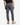 A person wearing the PROJEK RAW SOLID BUNGEE PULL ON JOGGER in gray with a relaxed fit, paired with a black shirt and beige boots, is standing with their back to the camera against a plain, light background.