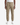 A person is wearing the PROJEK RAW SOLID BUNGEE CARGO CLASSIC FIT JOGGER, tan cargo jogger pants with stretch fabrication, cargo pockets, and a drawstring waist, paired with white sneakers, standing against a white background.