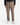 A person wearing the PROJEK RAW SOLID BUNGEE RELAXED FIT CARGO PANT for men, featuring utility pockets in tan, paired with a black long-sleeve shirt and white sneakers, stands against a plain white background.