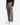 A person wearing PROJEK RAW SOLID BUNGEE RELAXED FIT CARGO PANT in tan with utility pockets, paired with a black long-sleeve shirt and white sneakers, stands against a plain white background.