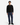A man stands facing forward against a plain white background, wearing a black sweater, black shoes, a silver necklace, a watch, and the PROJEK RAW SOLID BUNGEE LOOSE FIT CARGO PANT for men in blue, featuring utility pockets and stretch fabric.