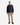 A man stands facing forward against a plain white background, wearing a blue plaid jacket, PROJEK RAW SOLID BUNGEE 5-POCKET RELAXED FIT PANTS in beige made from a premium stretch blend, and black sneakers.