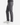 A person stands sideways with hands in their pockets, wearing the PROJEK RAW SOLID BUNGEE 5-POCKET RELAXED FIT PANTS in gray and white sneakers, set against a white background.