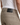 A person wearing PROJEK RAW SOLID BUNGEE 5-POCKET RELAXED FIT PANTS in beige, featuring a black leather patch label, paired with a white ribbed tank top. The image highlights the back waist area and the classic 5-pocket design of the pants.