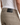 A person is shown from the back wearing PROJEK RAW’s SOLID BUNGEE 5-POCKET RELAXED FIT PANTS in beige, paired with a white ribbed tank top. The focus is on the waist and back pocket area, highlighting a black leather patch with subtle text on the waistband of these contemporary essential pants.