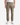 A person wearing PROJEK RAW SOLID BUNGEE 5-POCKET RELAXED FIT PANTS in light brown, paired with white sneakers and standing against a plain white background. The pants, designed as a modern essential, feature both front and back pockets. The person’s arms are relaxed at their sides.