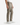 A man wearing PROJEK RAW SOLID BUNGEE 5-POCKET RELAXED FIT PANTS and white sneakers stands against a white background. Only his lower torso and legs are visible, with his arms resting by his sides.