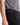 A person wearing PROJEK RAW’s SOLID BUNGEE 5-POCKET RELAXED FIT PANTS in black, featuring a visible black leather patch on the waistband, paired with a gray shirt adorned with a black abstract pattern. Only the torso and upper thigh are shown, highlighting these modern essentials.