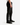 A man is wearing PROJEK RAW’s CAVALRY TWILL BUNGEE CHINO PANTS, paired with black sneakers and a white shirt. He stands against a plain white background in a relaxed pose, showing his left side.