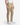 A person wearing PROJEK RAW CAVALRY TWILL BUNGEE CHINO PANTS in beige, paired with a white sleeveless shirt and white sneakers, stands against a plain white background—effortlessly blending modern office dressing with classic style.