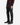 A person is standing against a white background, showcasing only their lower torso and legs while wearing PROJEK RAW CAVALRY TWILL BUNGEE 5-POCKET PANTS in dark gray, paired with black dress shoes and a burgundy sweater.