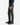 A person wearing PROJEK RAW PLAID BUNGEE CLASSIC FIT CHINO PANTS, paired with black dress shoes and a dark long-sleeve shirt, stands sideways with their left hand relaxed at their side against a plain white background.