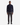 A man stands facing forward against a plain white background, wearing a navy half-zip sweater, PROJEK RAW MINI HOUNDSTOOTH TEXTURED BUNGEE CLASSIC FIT CHINO PANT in dark gray, and black shoes.