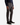 A person wearing the PROJEK RAW MINI HOUNDSTOOTH TEXTURED BUNGEE CLASSIC FIT CHINO PANT stands against a plain white background, paired with a dark navy sweater and black dress shoes.