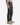 A man wears PROJEK RAW’s CANVAS BUNGEE CLASSIC FIT 5-POCKET PANTS in olive green, paired with a beige long-sleeve shirt and tan suede lace-up boots, standing against a white background for a refined workwear look.