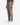 A person wearing PROJEK RAW KNIT CAVALRY TWILL RELAXED FIT CHINO PANTS in taupe and white sneakers stands against a plain white background. Only the lower half of the body is visible, highlighting the modern tailoring and relaxed-fit chino silhouette.