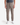 A person wearing PROJEK RAW’s KNIT CAVALRY TWILL RELAXED FIT CHINO PANTS in taupe with a drawstring waist, paired with a dark gray t-shirt and white sneakers, stands against a plain white background.
