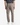 A person is shown from the back, standing against a white background and wearing PROJEK RAW’s KNIT CAVALRY TWILL RELAXED FIT CHINO PANTS in taupe, styled with white sneakers. These pants feature modern tailoring, an elastic waistband, and two back pockets.
