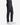 A person wearing classic-fit, dark PRATOFLEX CLASSIC FIT 5-POCKET PANTS by PROJEK RAW, paired with a dark sweater and white sneakers, stands against a plain white background.