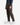 A person wearing PROJEK RAW’s CORDUROY RELAXED FIT CHINO PANTS, paired with a dark long-sleeve shirt and white sneakers, stands against a plain background, showcasing a modern silhouette.