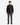 A person stands facing forward against a plain white background, wearing the PROJEK RAW CANVAS TWILL BUNGEE SHIRT in black, paired with gray pants and black shoes.