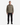 A man stands facing forward against a plain white background, wearing the PROJEK RAW TWILL OVERSHIRT in khaki—with front pockets, perfect for transitional weather—paired with black pants and black shoes.