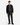 A person stands facing forward against a plain white background, wearing the PROJEK RAW BUNGEE SOLID ZIPPER OVERSHIRT—a black utility-inspired jacket—paired with a dark gray sweater, black cargo pants, and black lace-up shoes.