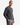 A man with short hair stands confidently against a plain background, wearing the PROJEK RAW SHAKER RIB CREWNECK SWEATER in dark gray paired with gray pants, one hand casually in his pocket.