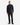 A man with short hair and a neutral expression stands against a white background, wearing the PROJEK RAW CLASSIC FIT CHENILLE PULLOVER 1/4″ ZIP SWEATER in navy, paired with black pants and black sneakers.