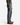 A person wearing a green sweater, PROJEK RAW BARU CLASSIC STRAIGHT FIT DENIM in washed indigo, and brown leather shoes stands against a plain white background, shown from the shoulders down in a side view.