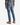 Wearing the PROJEK RAW BARU CLASSIC STRAIGHT FIT DENIM in a stone blue wash, along with a gray plaid shirt and tan boots, a person stands with their back to the camera against a white background.