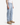 A person wearing the PROJEK RAW DREW BAGGY FIT DENIM, a white sleeveless shirt, and tan suede boots stands against a plain white background with their arms relaxed at their sides; their face is not visible.