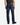 A person is standing with their back to the camera, wearing the PROJEK RAW ATLAS ATHLETIC FIT DENIM in a midnight blue wash and black shoes. The jeans feature a tapered leg, visible pockets, and a brown label on the waistband.