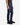 Wearing a brown shirt, the person models PROJEK RAW’s ATLAS ATHLETIC FIT DENIM in midnight blue wash with a tapered leg and black sneakers, standing against a white background, pictured from shoulder to foot and facing left.