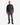 A man faces forward against a plain white background, wearing the MEN’S VEGAN LEATHER MOTO JACKET by PROJEK RAW, paired with gray jeans and black shoes.