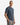 A man with short hair wears a dark blue PROJEK RAW CLASSIC CREWNECK T-SHIRT and gray jogger pants, standing with one hand in his pocket against a plain white background.
