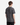A person stands facing away, wearing a PROJEK RAW PRINTED COTTON SINGLE JERSEY T-SHIRT in a short-sleeve, dark gray marbled style and black pants against a plain white background.