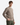 A young man wearing the PROJEK RAW RELAXED FIT KNIT CORD CREWNECK SWEATER in taupe and green pants stands with one hand in his pocket against a plain white background.