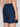 A person is shown from the waist down wearing Projek Raw BRUNO-NAVY swim shorts featuring a dark palm tree pattern, elastic waistband, and back pocket. Their left arm rests relaxed at their side.