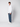 A young man with curly hair stands against a white background, wearing a white button-up shirt, PROJEK RAW Mens Bungee Relaxed Chino Pant, and white sneakers. He faces slightly to the side with a neutral expression.