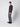 A young man with short curly hair stands against a light background, wearing a dark PROJEK RAW sweater, PROJEK RAW Mens 5-pocket Classic Stretch Bungee Pants in light gray, and black shoes. He looks slightly to the side with a neutral expression.