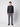 A young man stands against a light grey background, facing forward with a neutral expression. He wears a dark long-sleeve sweater, PROJEK RAW Mens 5-pocket Classic Stretch Bungee Pants, and black shoes.