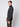 A young man with short light brown hair models the PROJEK RAW Mens Half-zip Cashmere Touch Sweater in dark gray and brown pants, standing sideways and looking at the camera against a plain light background.