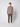 A young man stands against a light gray background, wearing a taupe button-up shirt, PROJEK RAW Mens Bungee Relaxed Chino Pant in dark brown, and white sneakers. He faces forward with a neutral expression, arms relaxed at his sides.