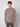 A young man with short curly brown hair wears the PROJEK RAW Mens 24/7 Button-up Shirt in taupe with matching pants, standing against a light gray background and looking directly at the camera with a neutral expression.