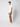 A young man stands against a light background, wearing a white t-shirt, PROJEK RAW Mens Bungee Relaxed Chino Pant in tan, and white sneakers, looking at the camera with a neutral expression.