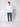 A man stands against a plain light background, wearing a white button-up shirt, PROJEK RAW Mens Bungee Relaxed Chino Pant in blue, and white sneakers. He faces forward with his arms relaxed at his sides.