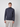 A young man with short light brown hair wears the PROJEK RAW Mens Long Sleeve Turtleneck Sweater in dark gray and light beige pants, standing against a plain light gray background.