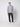 A young man stands against a plain light background wearing a light gray hoodie, PROJEK RAW Men’s 5-Pocket Pant in dark gray stretch fabric, and white sneakers. He faces the camera with a relaxed posture and neutral expression.